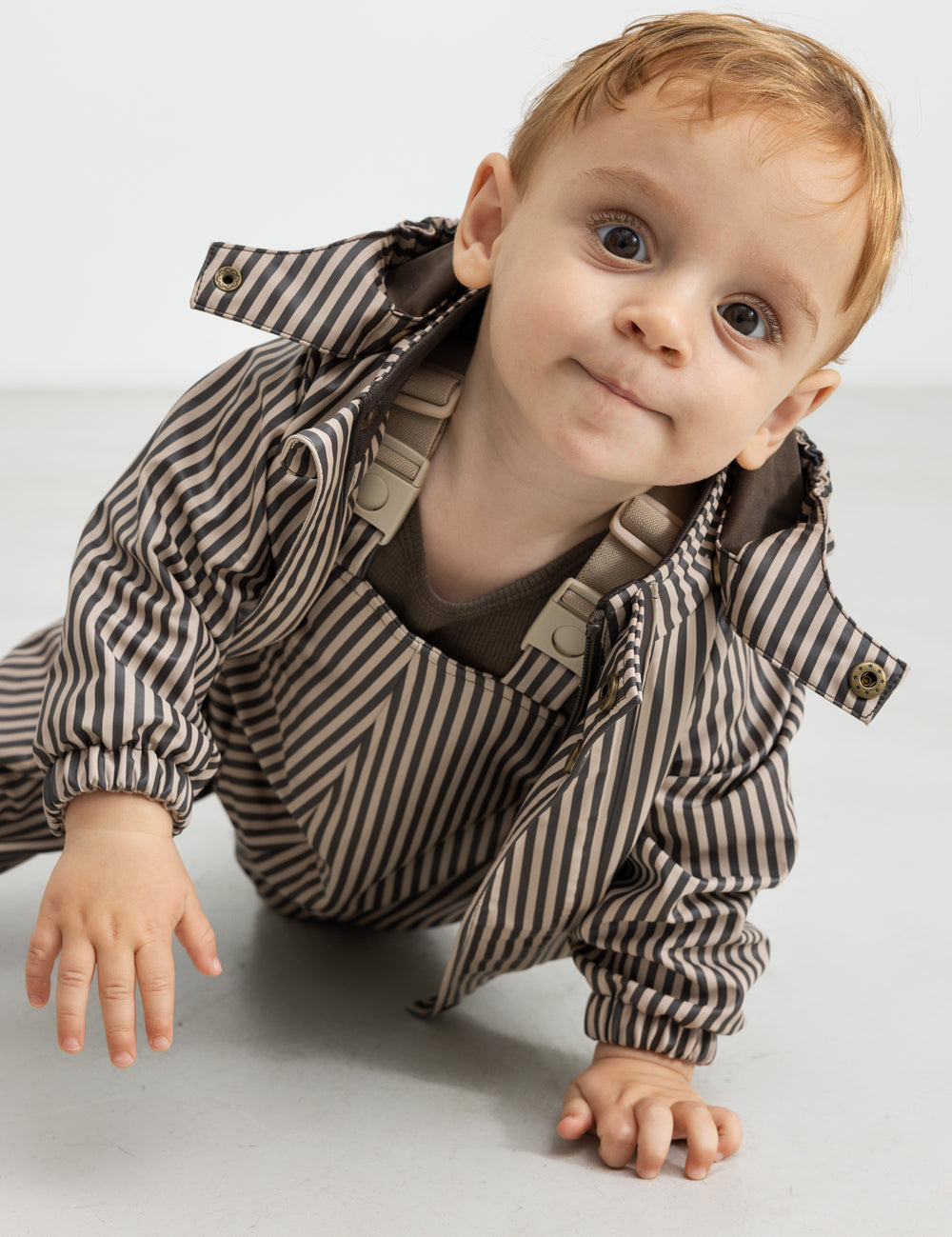 Barn i regnbueser med brune striber og jakke, kravler fremad