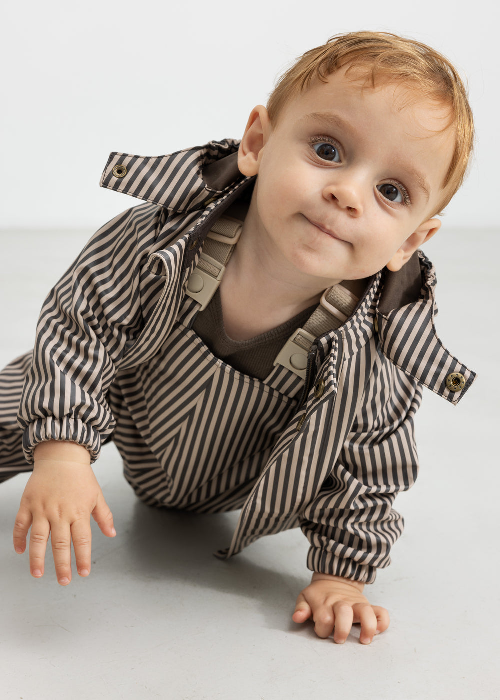 Baby i regnbukser med brune striber og jakke, kravler fremad