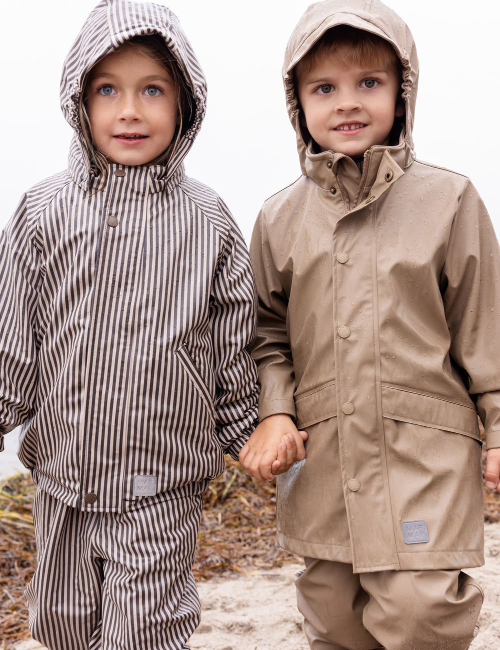 Børn iført regntøj, det ene barn bærer beige regnbukser og jakke.