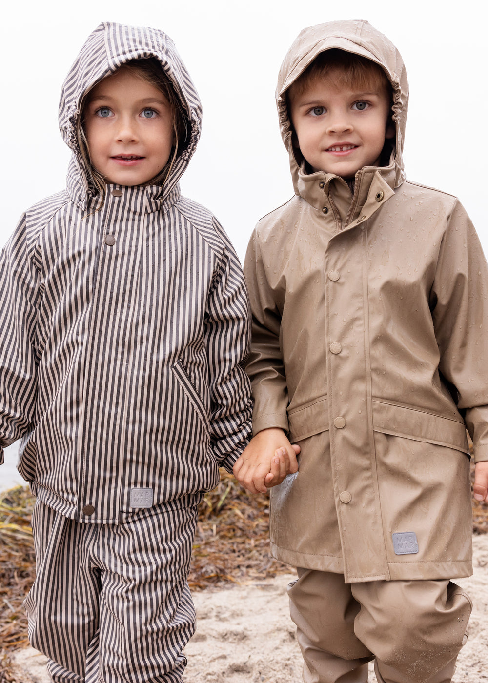 To børn iført regntøj på stranden, det ene barn i beige regnjakke og bukser