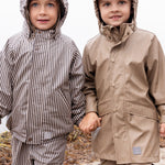 To børn iført regntøj på stranden, det ene barn i beige regnjakke og bukser