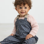 Barn iført mørkeblå regnbukser med print og lyserød trøje, sidder ned