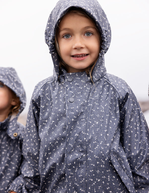 Barn iført regnjakke med hætte og blomsterprint