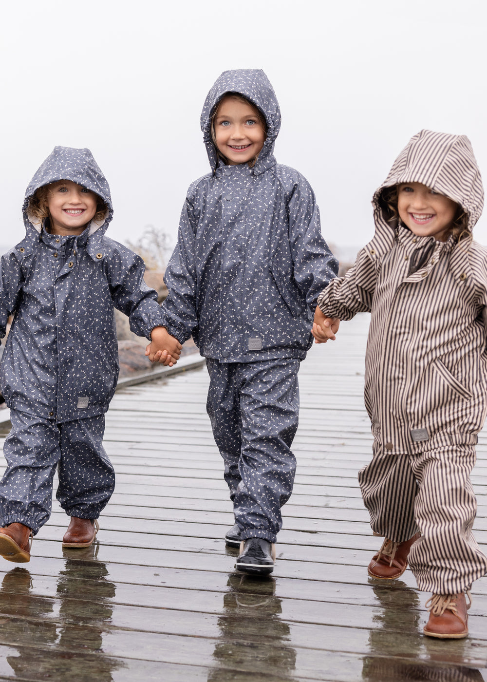 Tre børn i regntøj, midterste barn iført mørkeblåt sæt med print og hætte