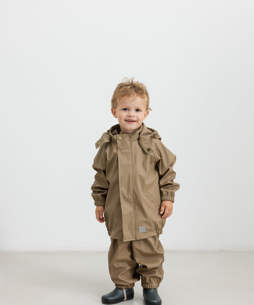 Barn iført beige regnsæt og gummistøvler, står og kigger op