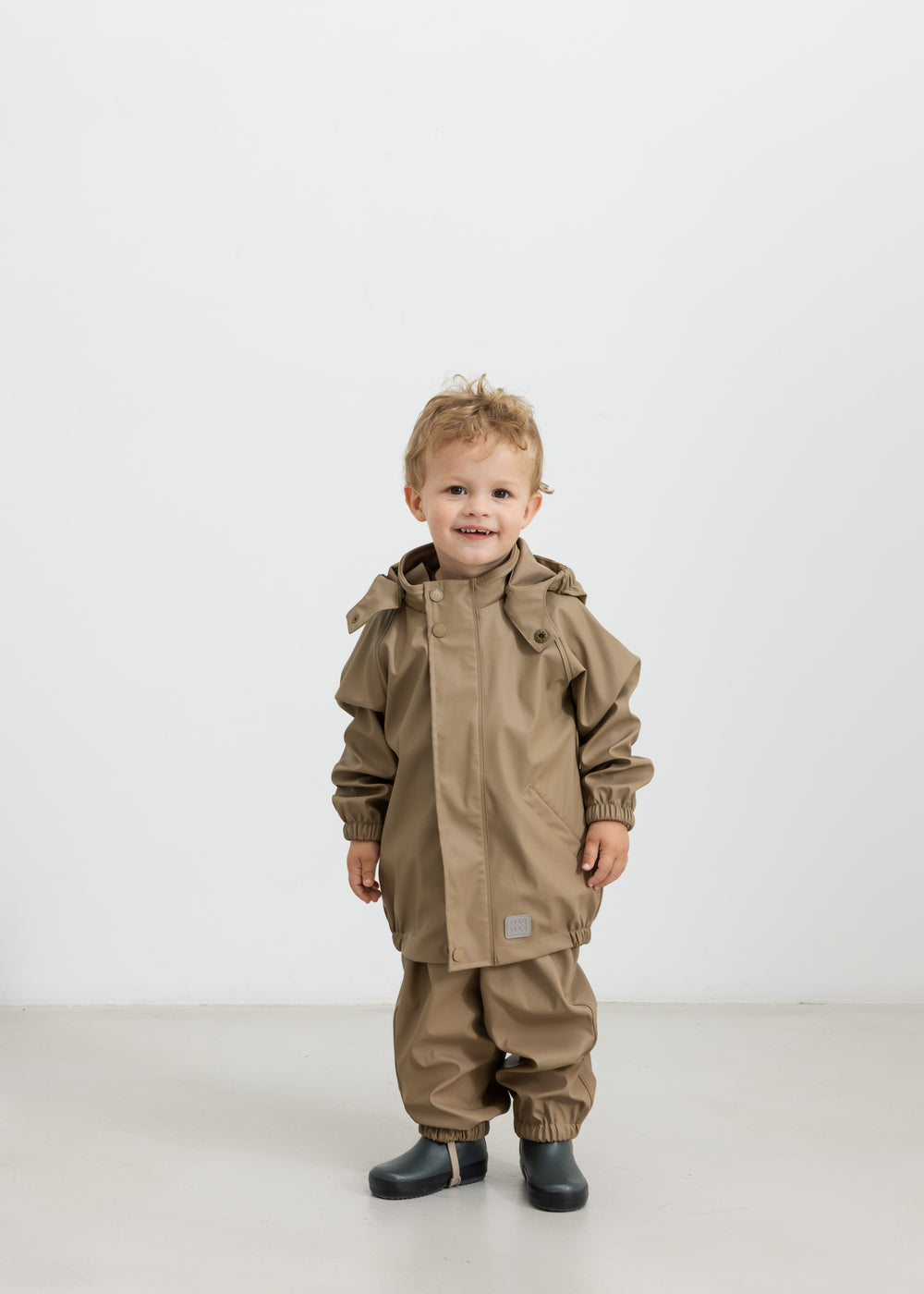 Barn iført beige regnsæt og gummistøvler, står og kigger op