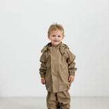 Barn iført beige regnsæt og gummistøvler, står og kigger op