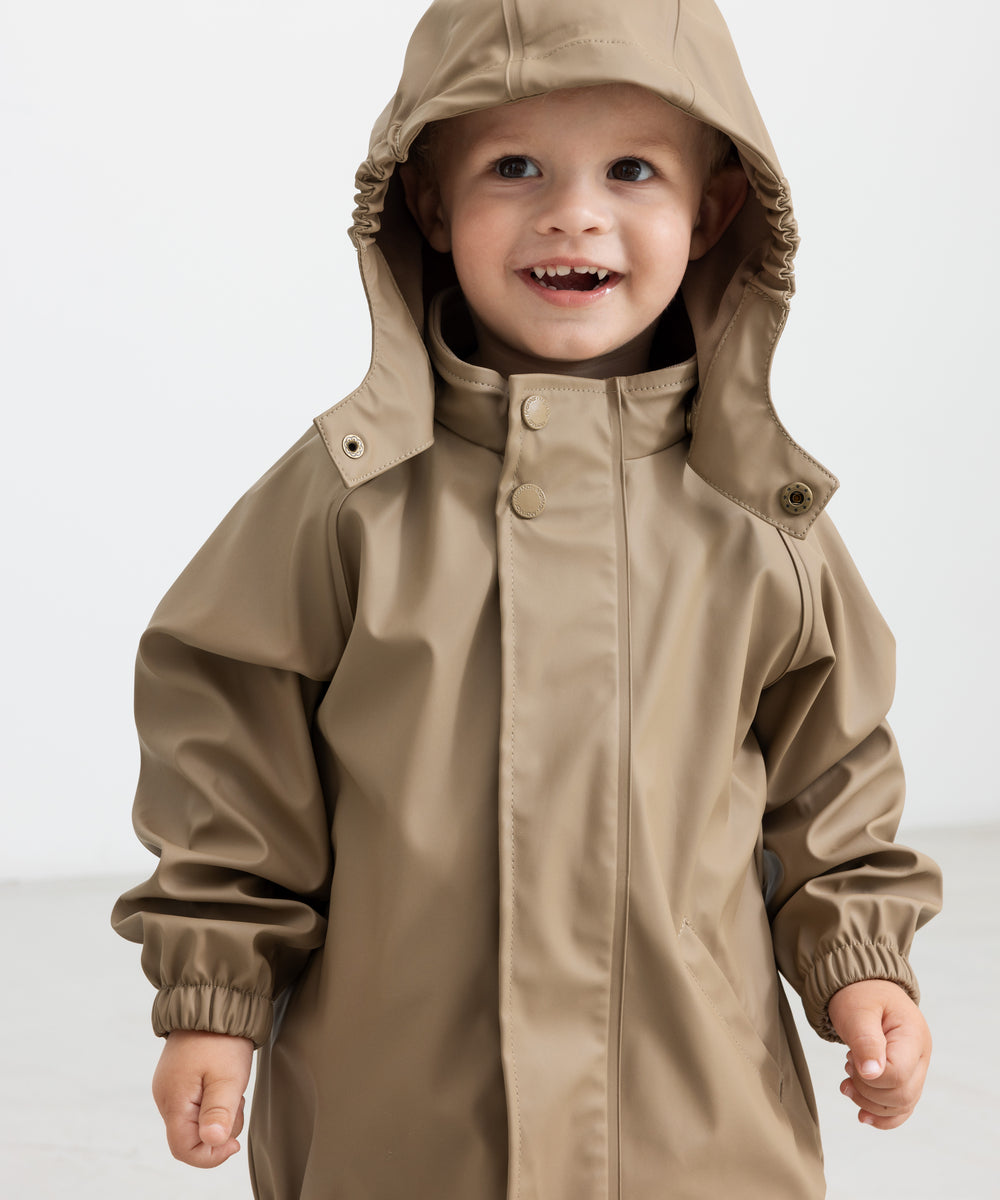 Barn iført beige regnsæt med hætte oppe, smilende