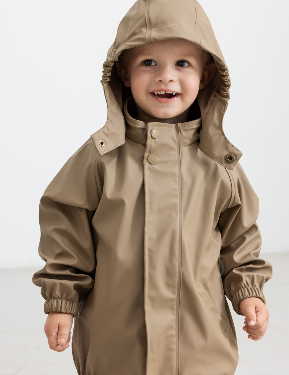 Barn iført beige regnsæt med hætte oppe, smilende