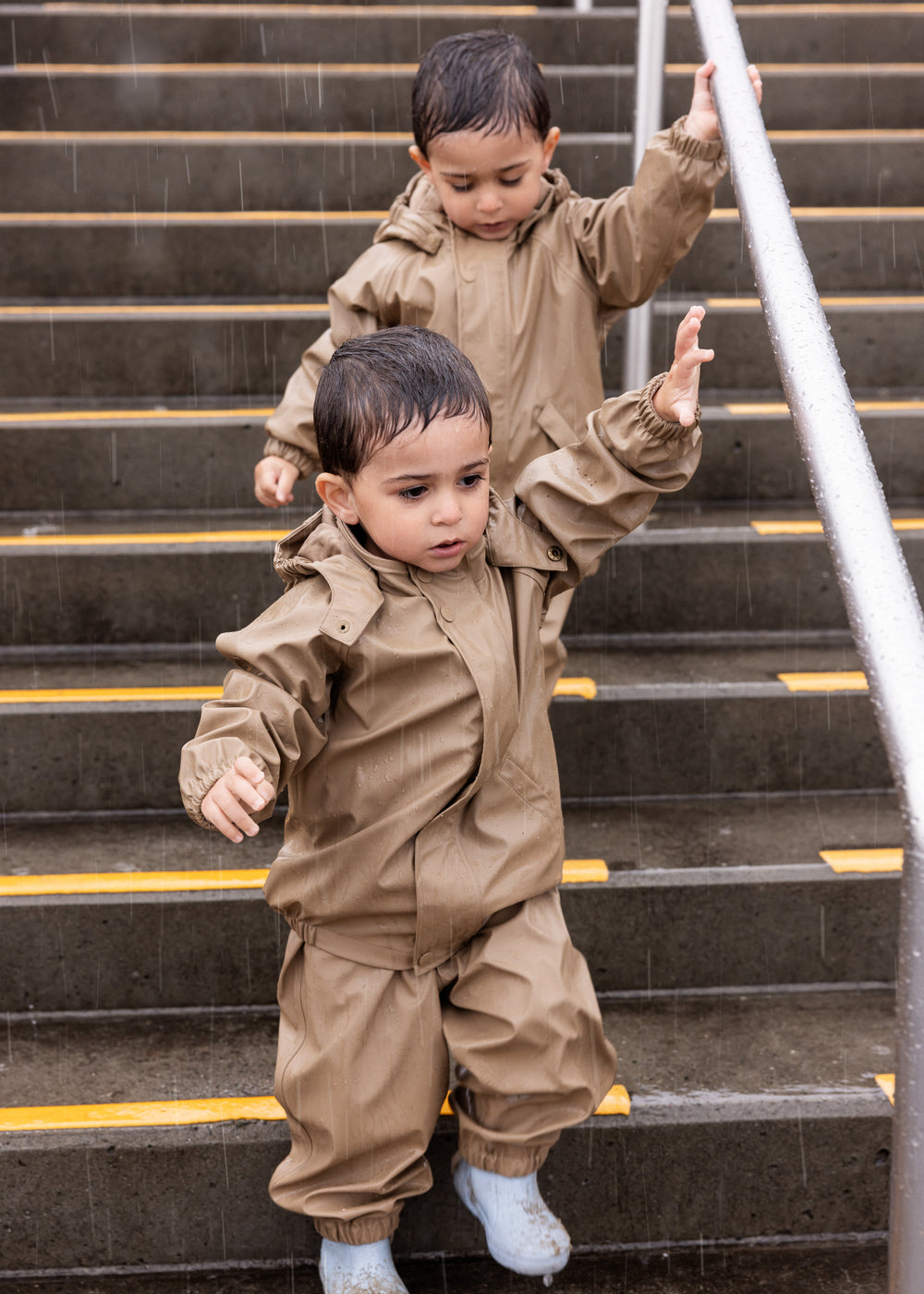 Tre børn på trappe, to iført beige regnsæt 