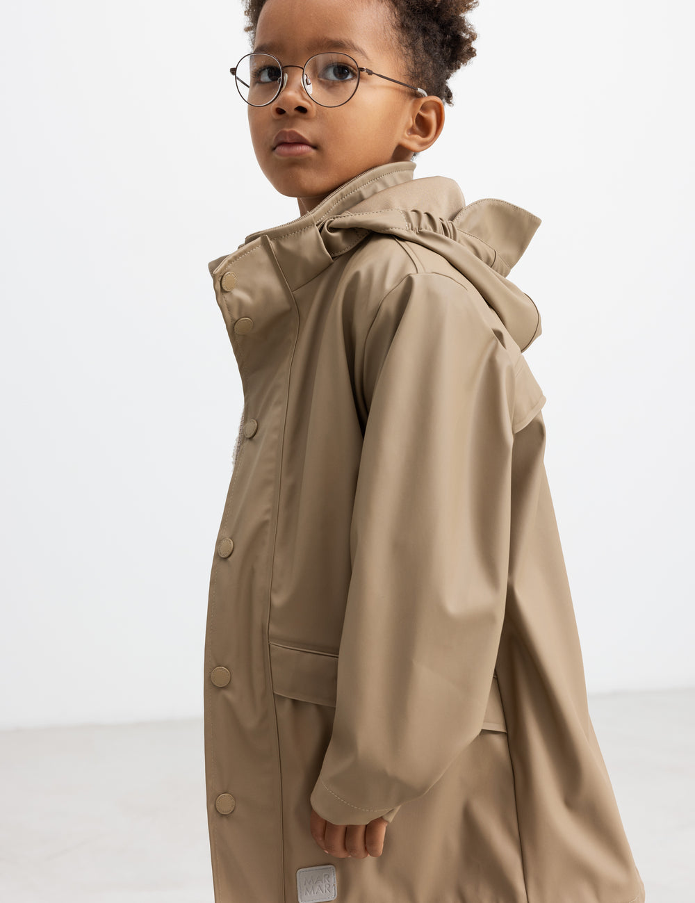 Barn iført beige regnjakke, set i profil med hætten oppe