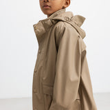 Barn iført beige regnjakke, set i profil med hætten oppe