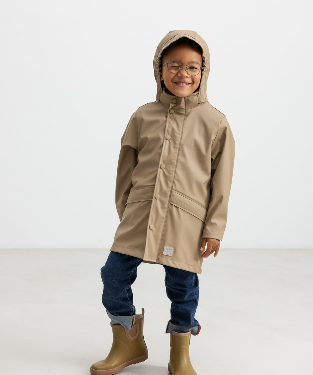 Barn iført beige regnjakke og gummistøvler, smilende