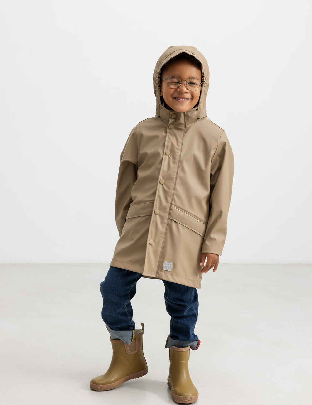Barn iført beige regnjakke og gummistøvler, smilende