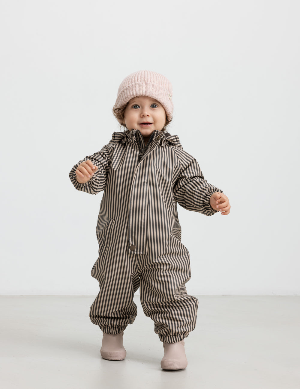 Lille børn i brun og hvid stribet regndragt med hætte og elastikstropper