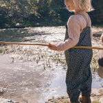 Børn iført mørkegrå regnbukser med prikker ved sø