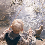 Dreng sidder ved sø iført brune stribede regnbukser