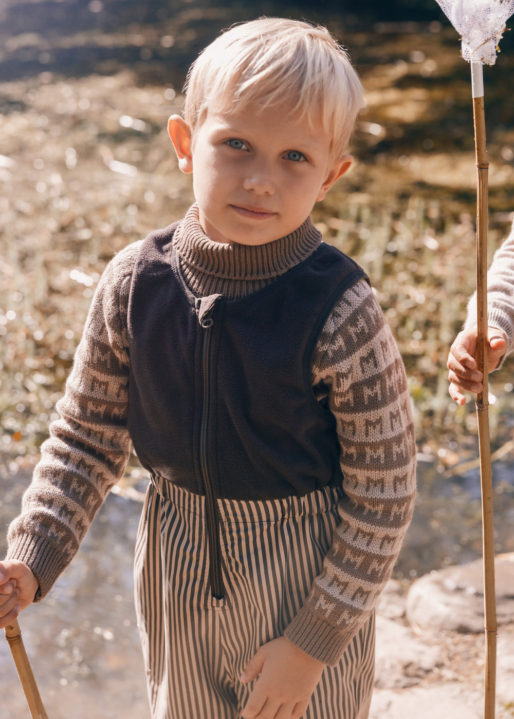 Dreng i brune stribede regnbukser med net i naturen