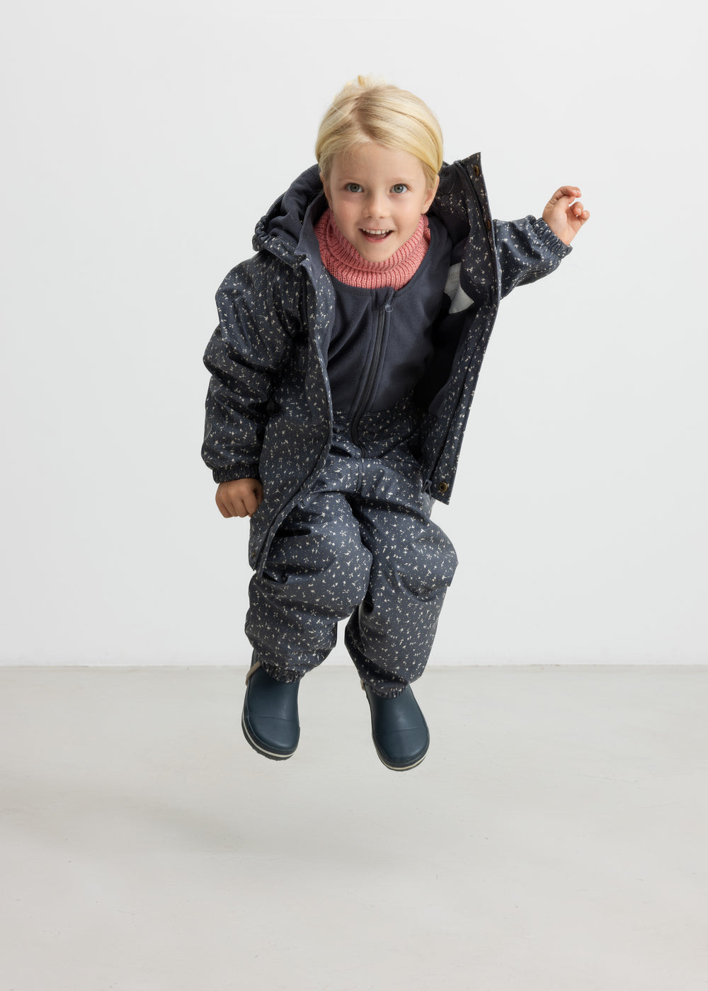 Børn hopper iført mørkegråt regnsæt med prikker og lyserød trøje