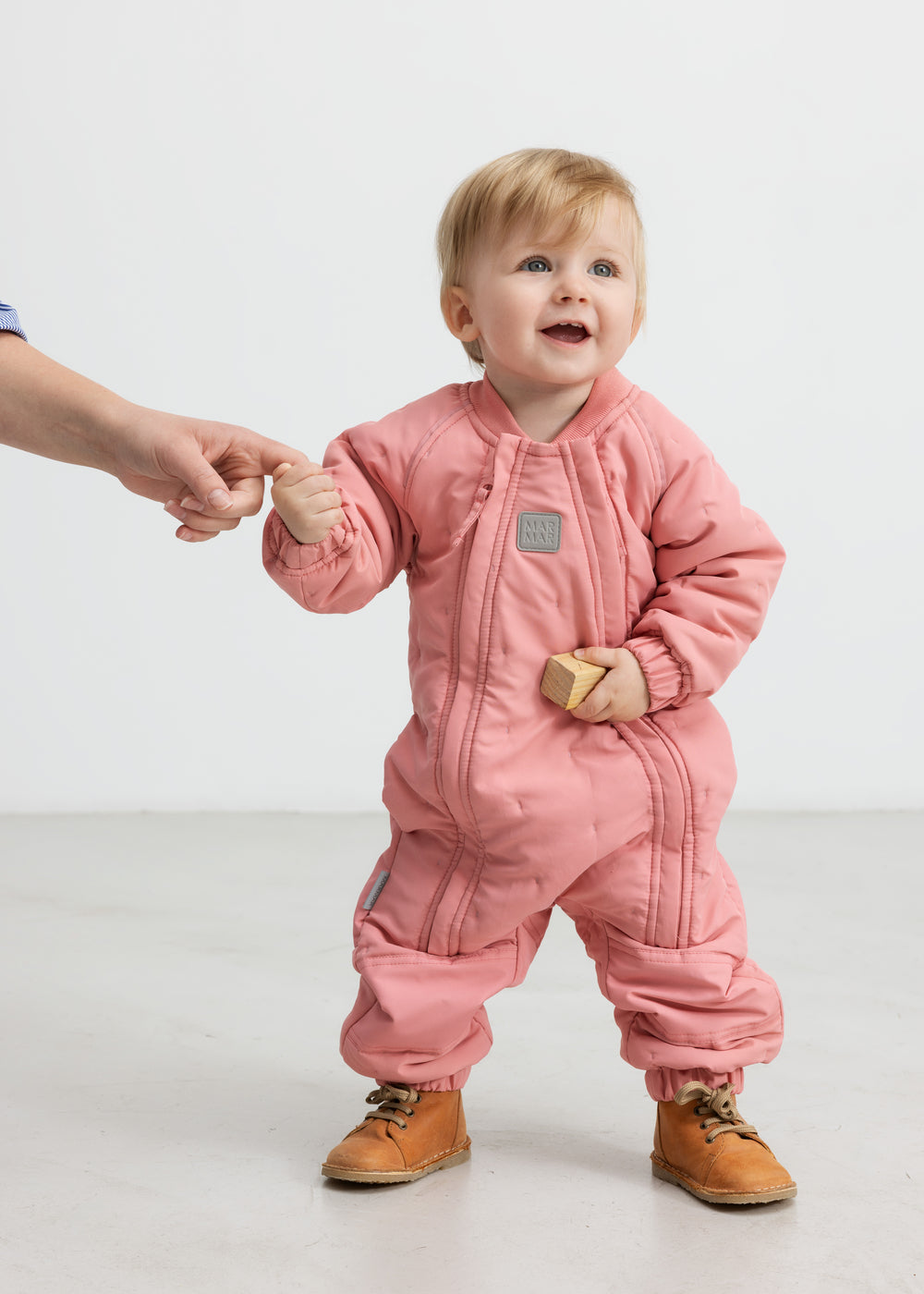 Baby iført lyserød termodragt, holder en voksen i hånden og smiler