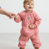 Baby iført lyserød termodragt, holder en voksen i hånden og smiler