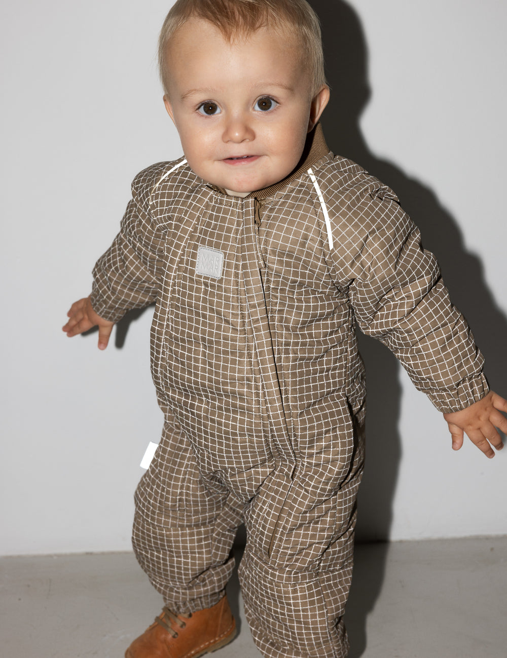 Baby iført brunternet termodragt, smilende og i bevægelse