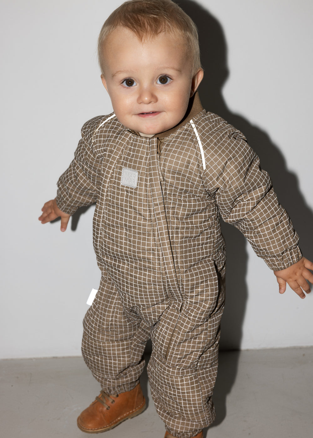 Baby iført brunternet termodragt, smilende og i bevægelse