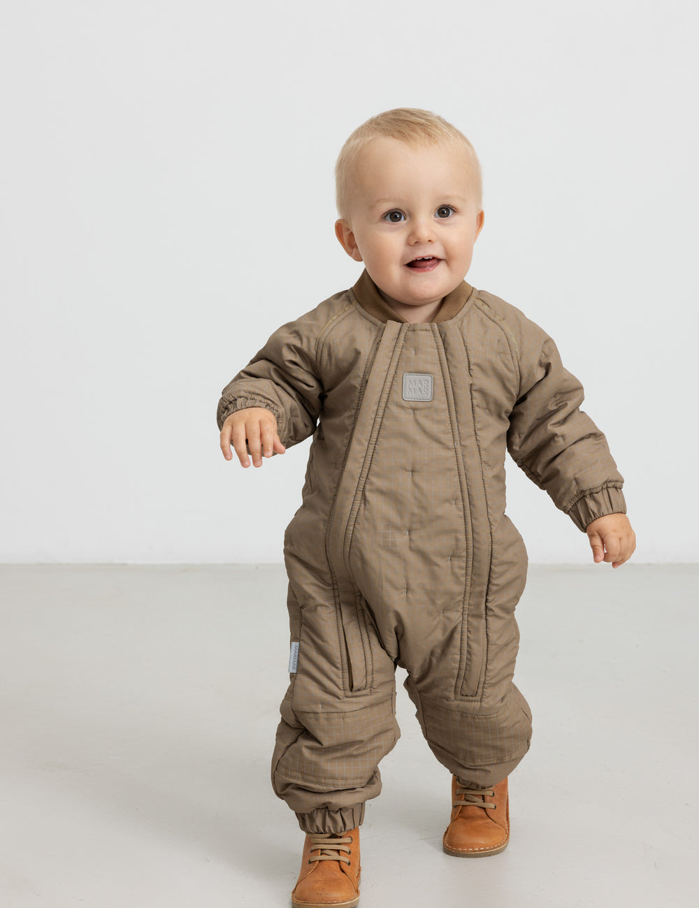 Baby iført brunternet termodragt, går mod kameraet