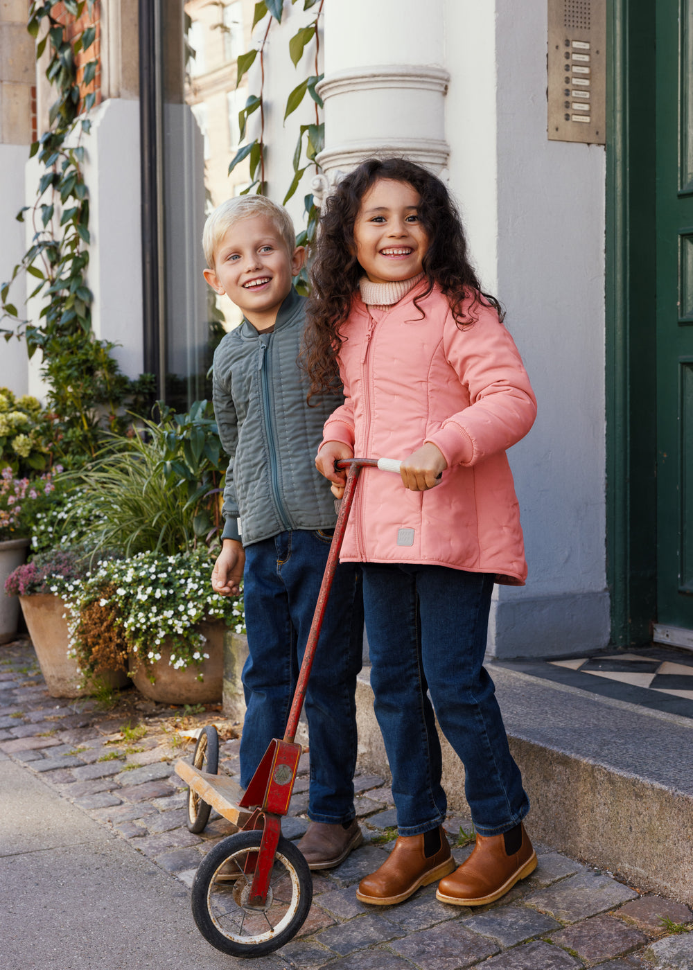 Pige i lyserød termojakke står med scooter ved siden af en dreng