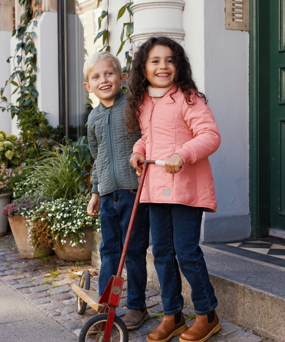 To børn foran en dør, dreng iført støvet grøn termojakke, pige i lyserød