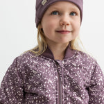 Barn iført lilla ribbeanie og jakke med print, smiler