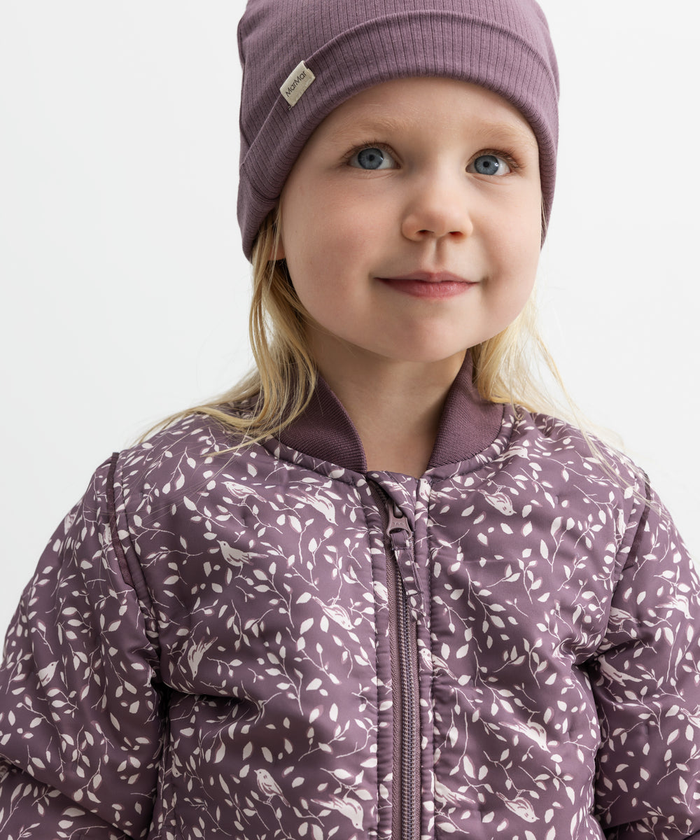 Barn iført støvlilla termojakke med hvidt bladmønster og matchende hue