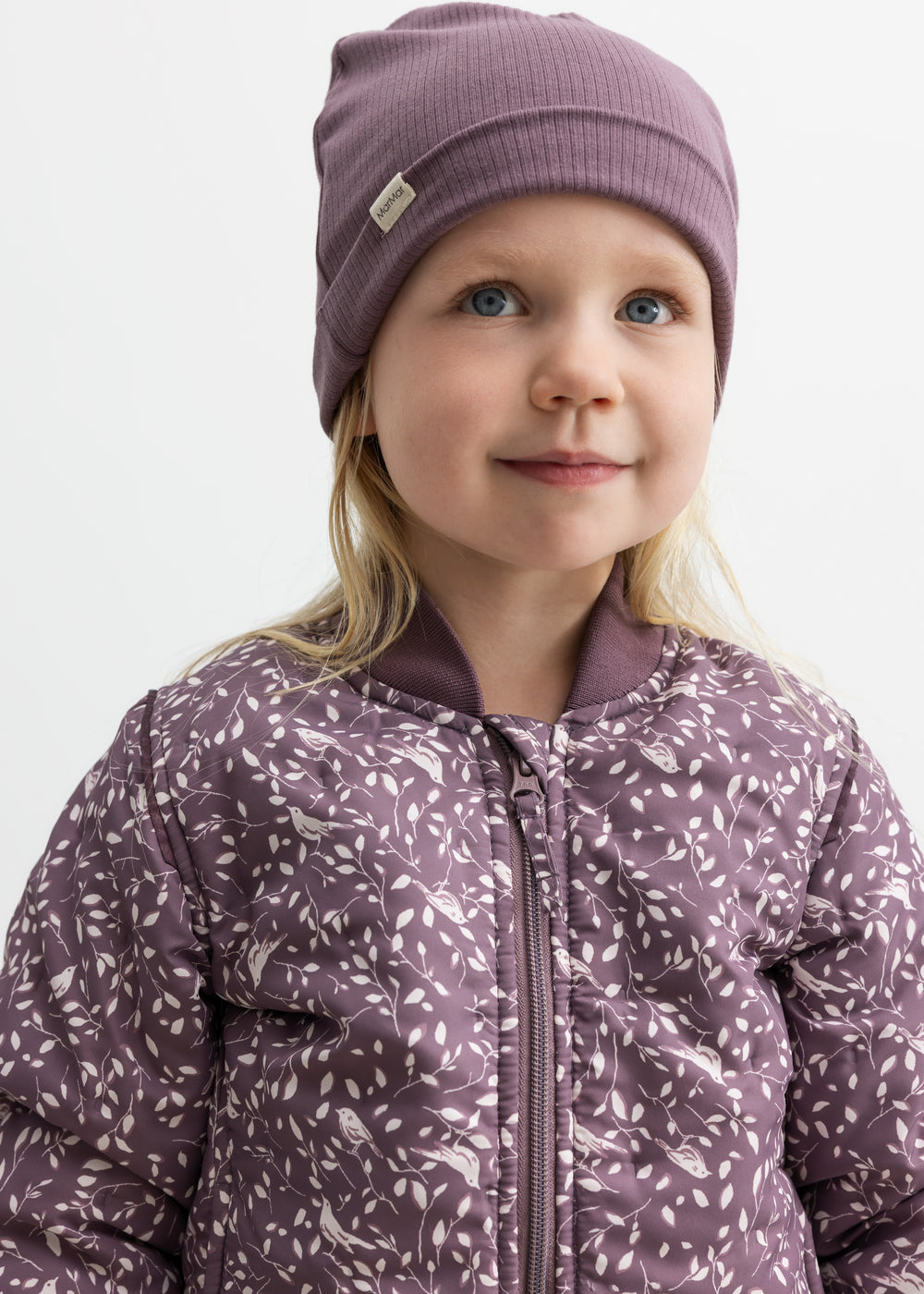 Barn iført støvlilla termojakke med hvidt bladmønster og matchende hue