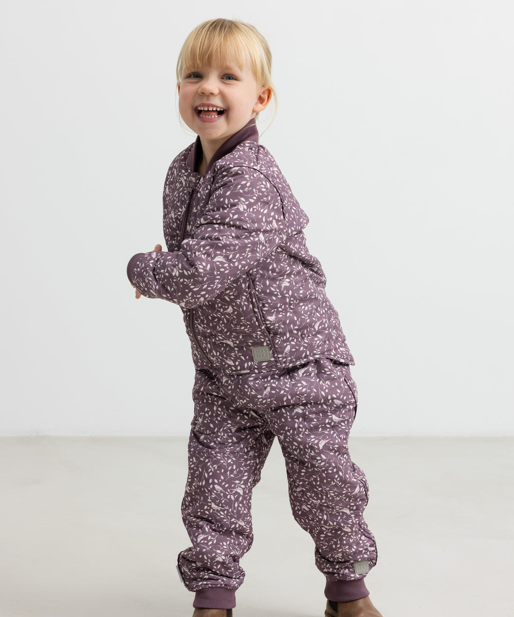 Barn iført støvlilla termotøj med print, smilende og i bevægelse