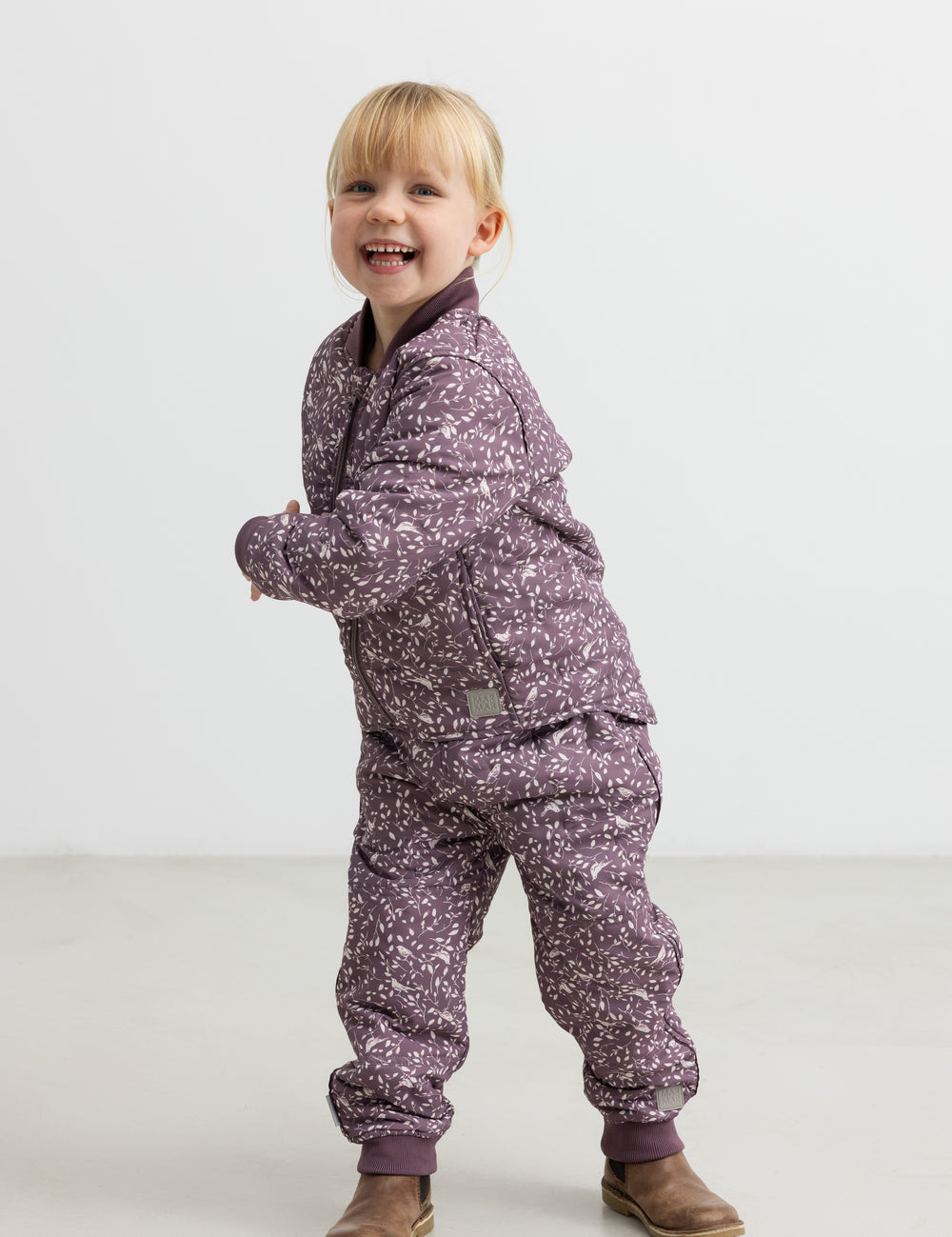 Barn iført støvlilla termotøj med print, smilende og i bevægelse