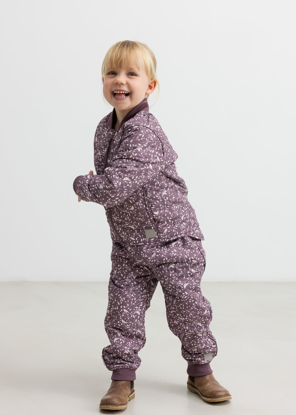 Barn iført støvlilla termotøj med print, smilende og i bevægelse