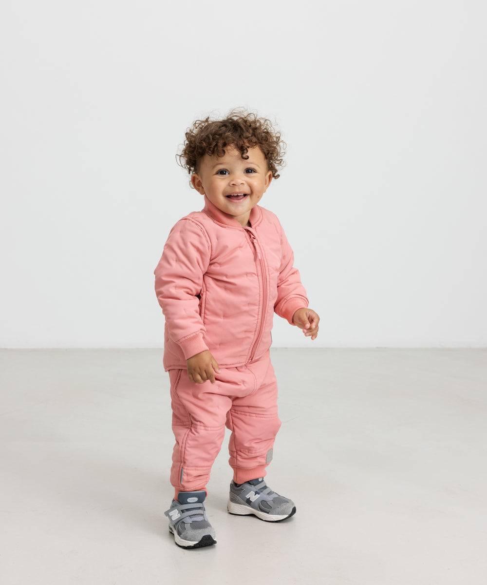 Lille barn iført lyserødt termotøj, smilende og i bevægelse