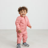 Lille barn iført lyserødt termotøj, smilende og i bevægelse