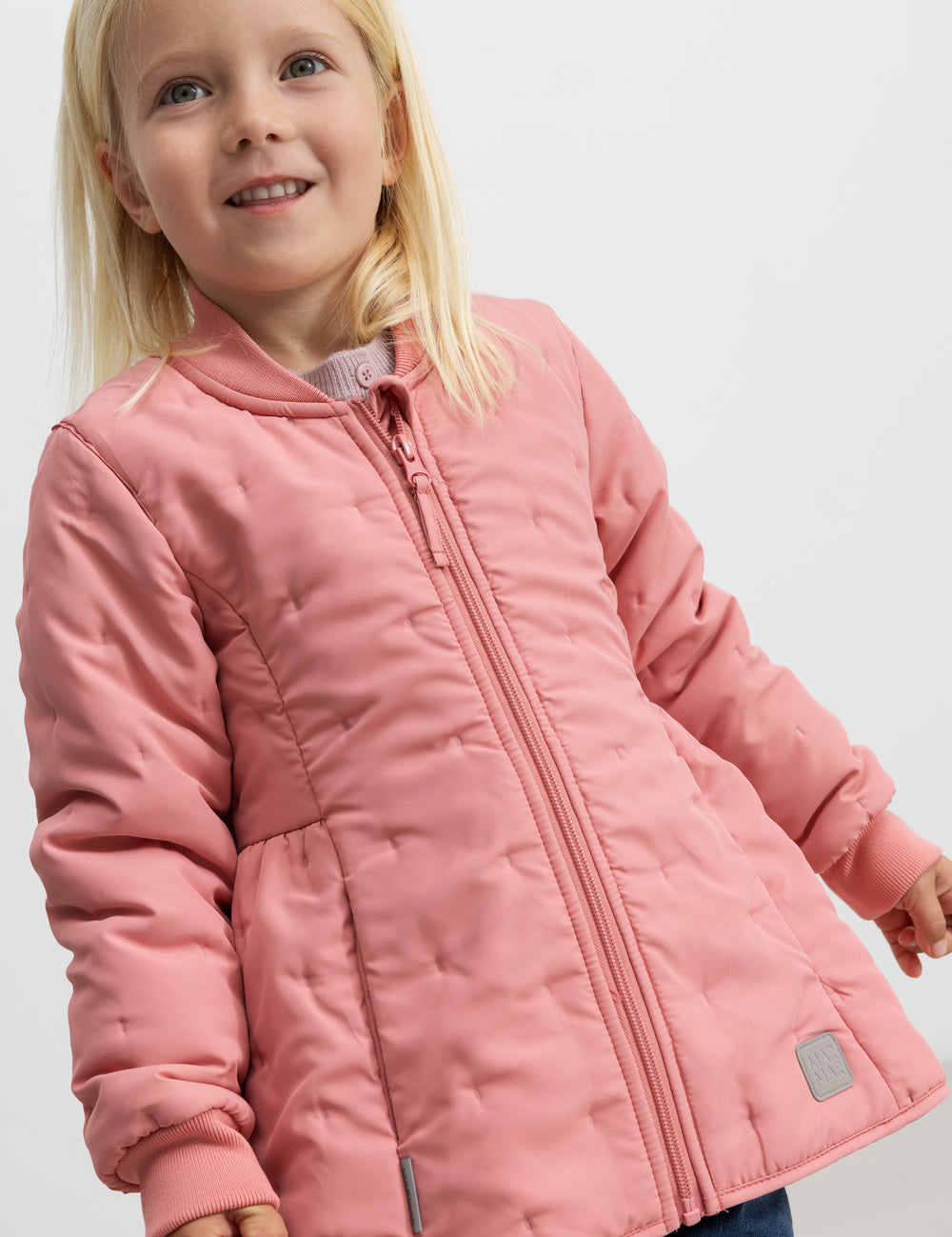 Barn iført lyserød termojakke, smilende og med hånden i lommen