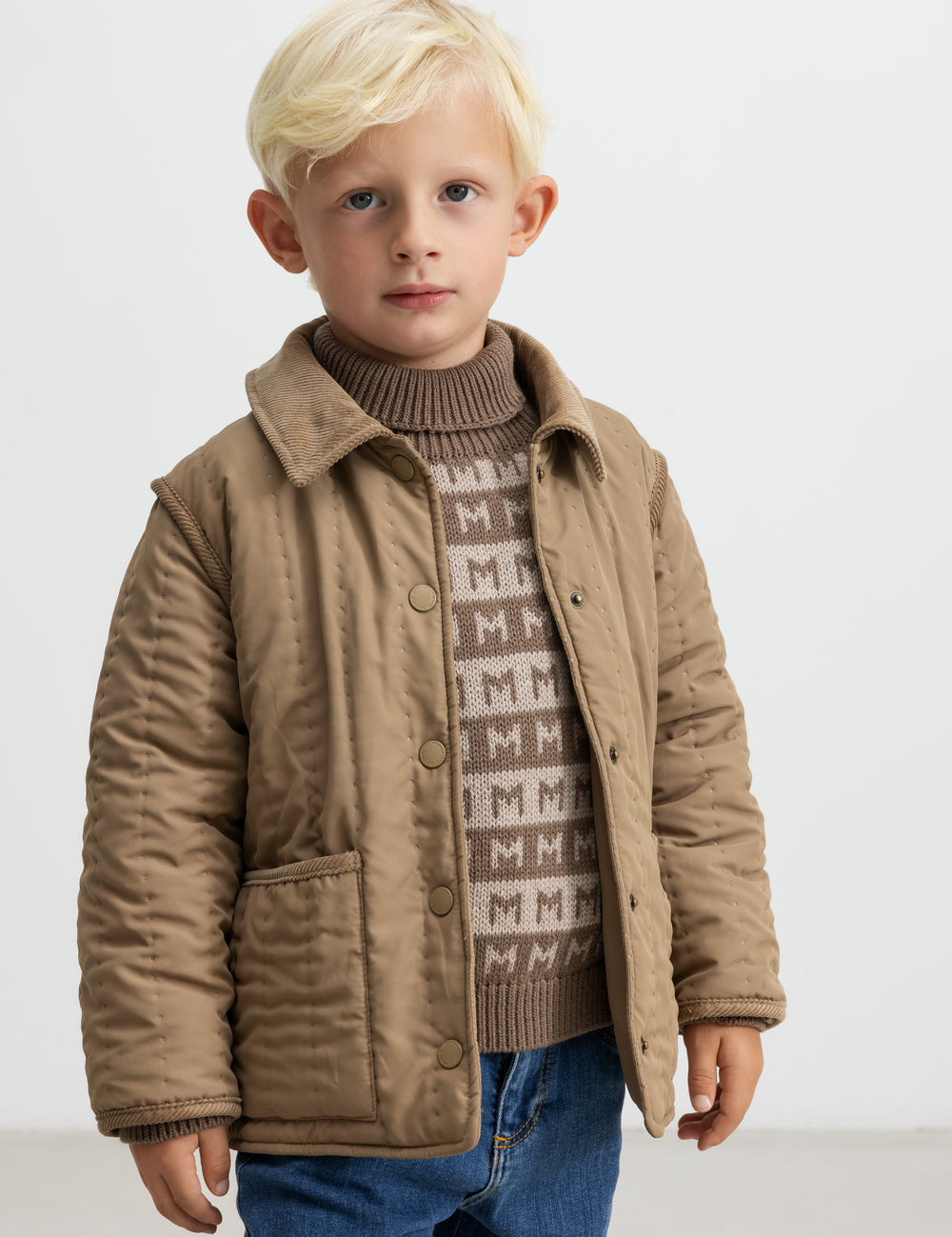 Barn iført brun termoakke og mønstret strik, kigger mod kameraet.
