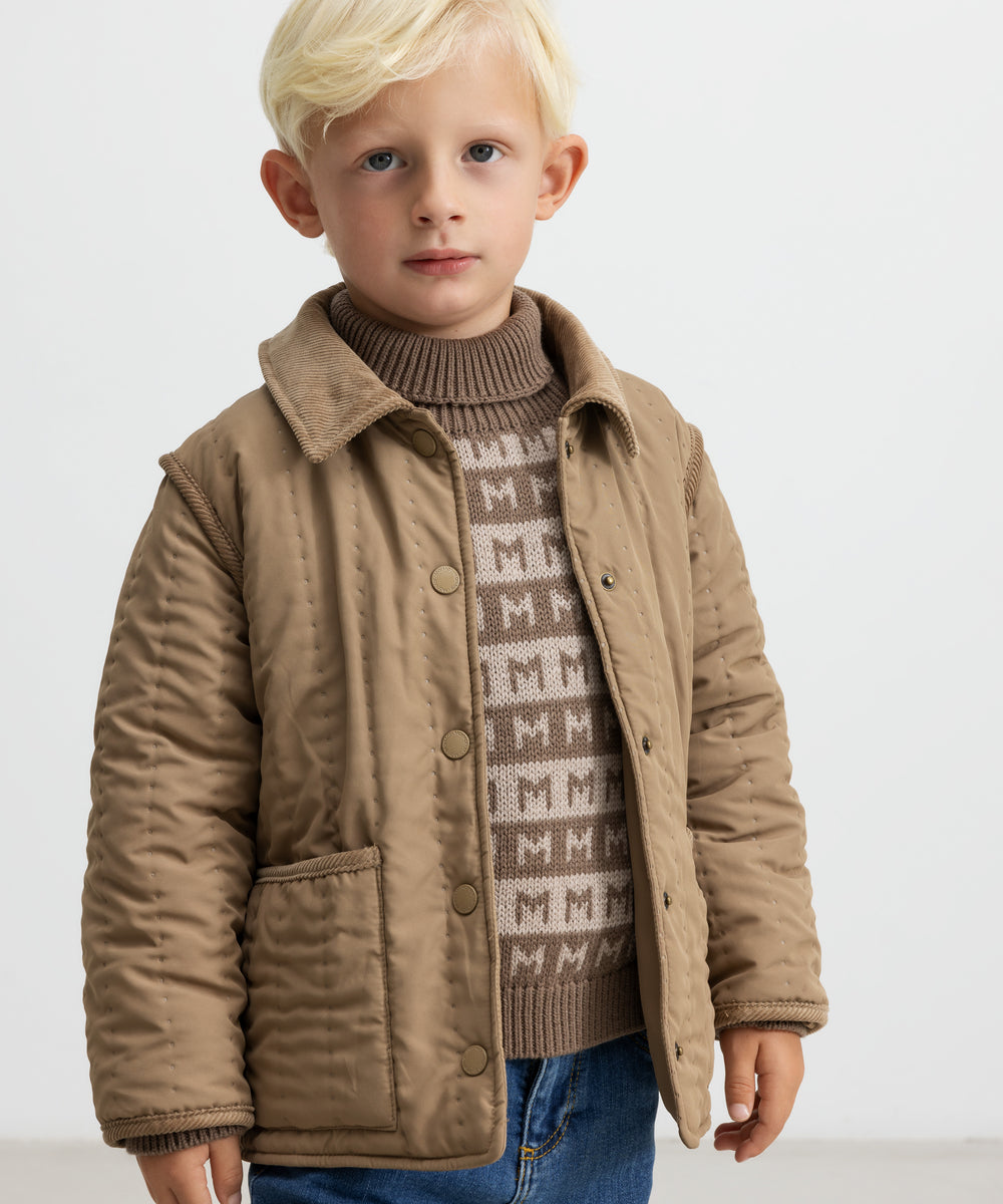 Barn iført brun striktrøje med M-mønster og quiltet jakke udenpå