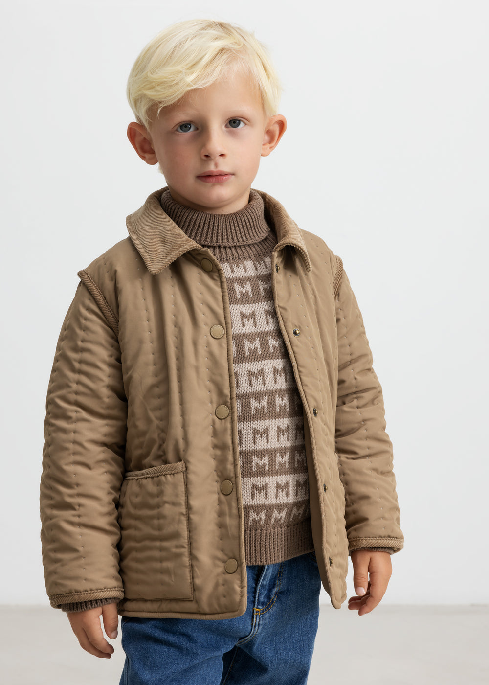 Barn iført brun striktrøje med M-mønster og quiltet jakke udenpå