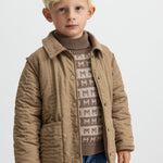 Barn iført brun striktrøje med M-mønster og quiltet jakke udenpå