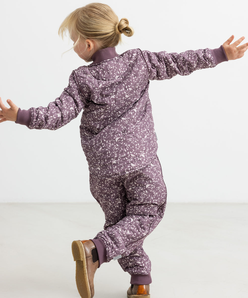 Barn iført støvlilla termojakke og bukser med print, hopper med armene ud