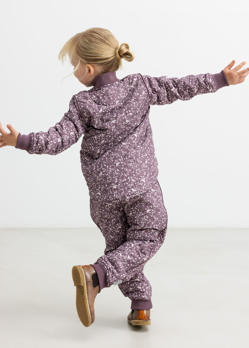 Barn iført støvlilla termojakke og bukser med print, hopper med armene ud