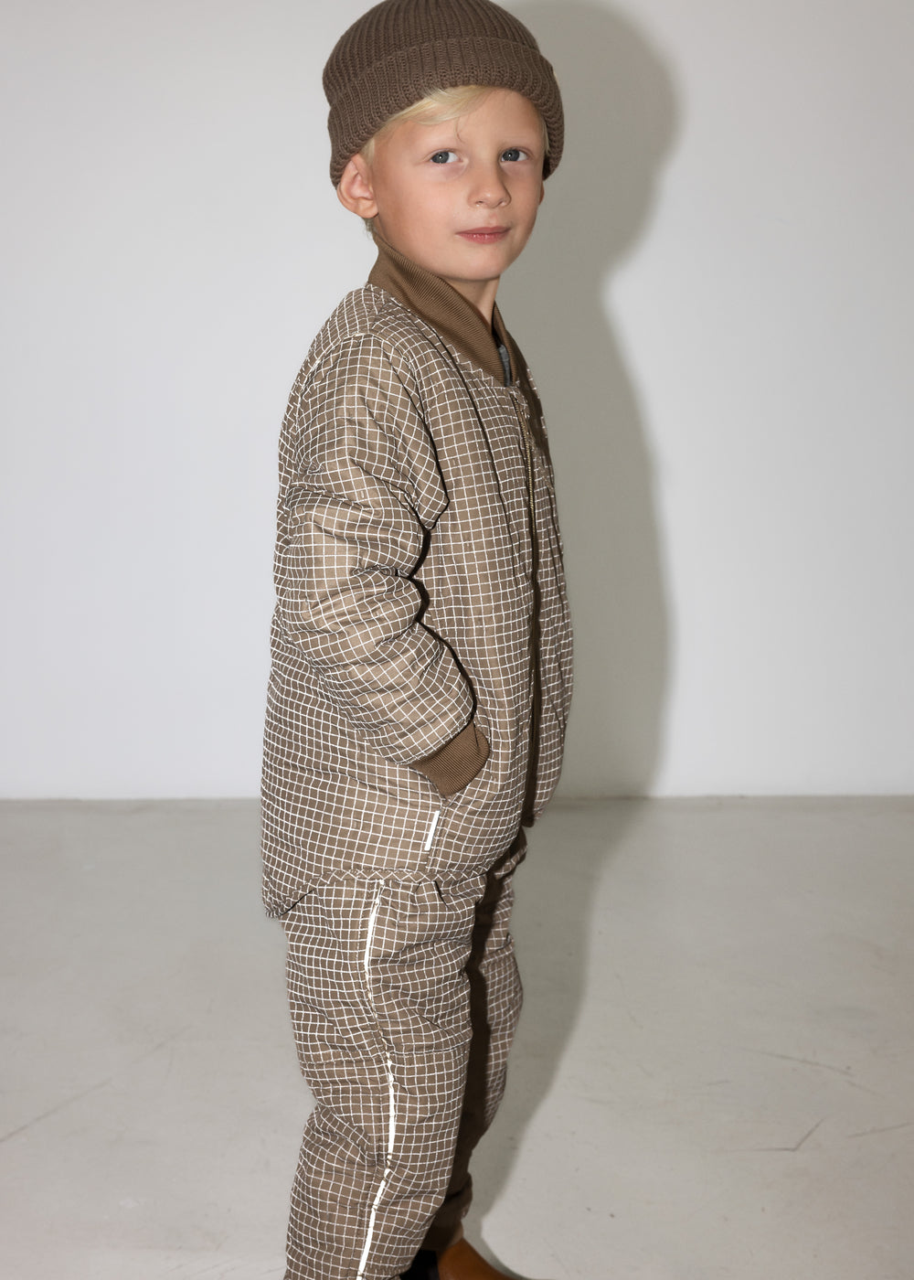 Dreng iført brunternet termojakke og hue, står i profil