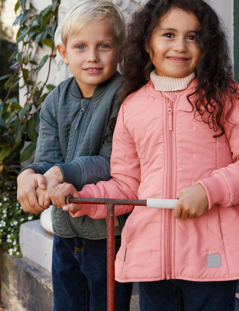 Pige i lyserød termojakke står med scooter ved siden af en dreng
