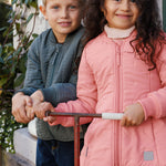 Pige i lyserød termojakke står med scooter ved siden af en dreng