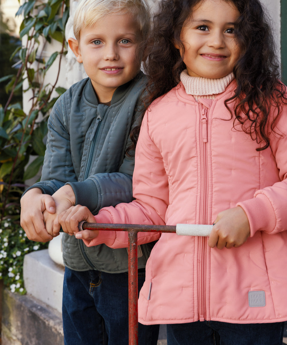 o børn holder en scooter, drengen iført støvet grøn termojakke og pigen lyserød