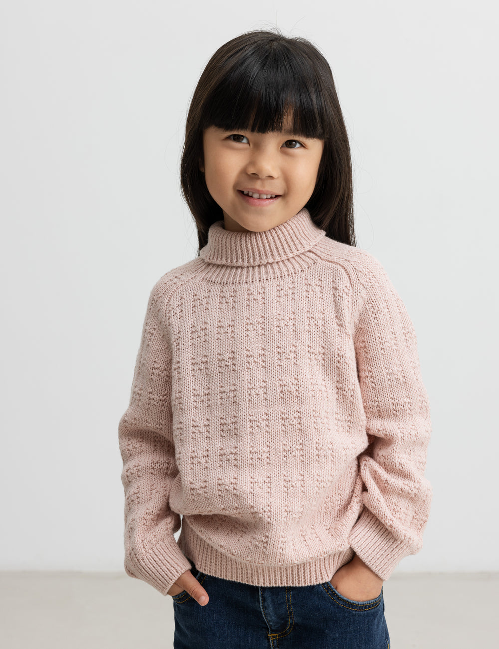 Barn iført lyserød striktrøje med rullekrave og mørkeblå jeans, smilende